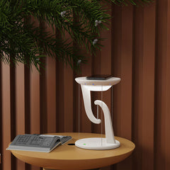 White lamp on a wooden table with a brown curtain and greenery in the background